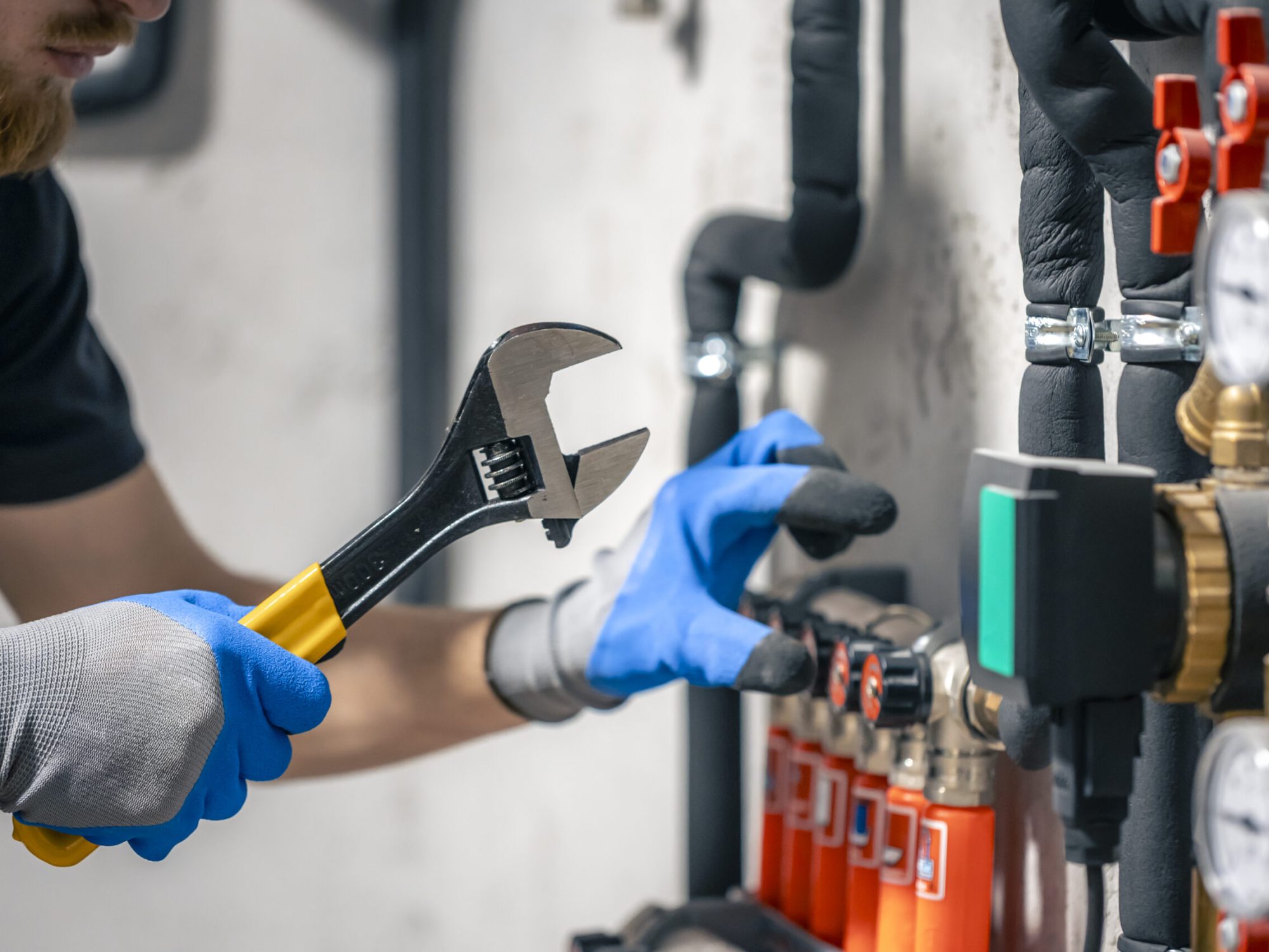 A man installs a heating system in a house and checks the pipes with a wrench. Adjusting heating valves in a residential building. A plumbing and heating technician works.